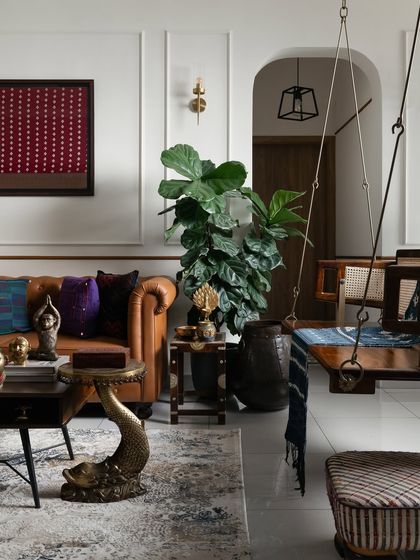 I love creating spaces that feel layered with history and personality. This living room corner features a classic tan leather sofa, a traditional wooden swing, and unique brass decor like the fish-shaped table. It’s a celebration of Indian craft and modern comfort, all in one frame.