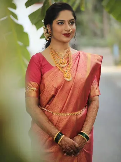 A beautiful bride ready for her engagement pooja, styled in a South Indian-inspired look with a gorgeous silk saree and layered necklaces.