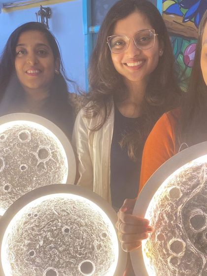 A group of friends beaming with pride as they show off their finished moon lamps. These workshops are a great way to learn a new skill and have fun together.
