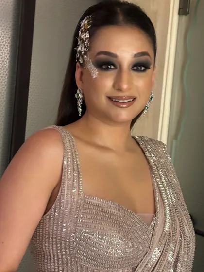 The client is glowing in her finished look. The sleek hair and dramatic accessory create a perfect balance with her shimmery outfit.