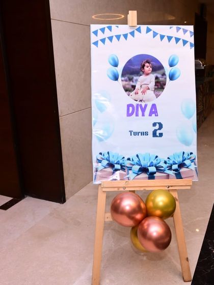 A welcome sign for a second birthday party, featuring the birthday girl's photo. The sign is placed on an easel and decorated with balloons to match the party theme.