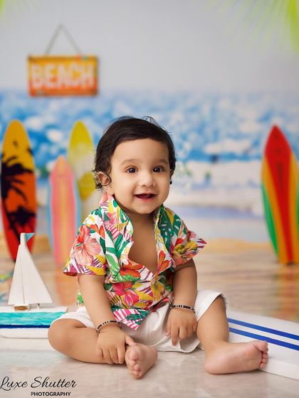 A bright and happy portrait of the baby boy in his colorful beach outfit, sitting on a surfboard prop.