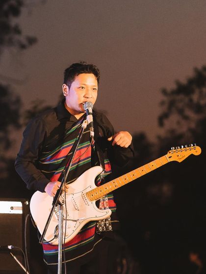 A guitarist sings passionately into the microphone during a live band performance. This candid shot captures the artist completely lost in their music.