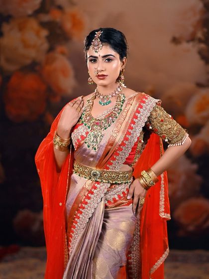 A classic bridal pose showcasing the elegance of the saree and the detailed craftsmanship of the jewelry. The painted backdrop provides a timeless and artistic setting.