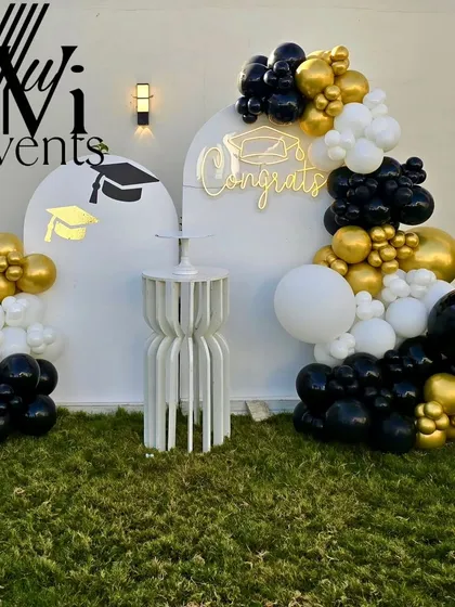 A stylish black, white, and gold balloon decoration for a graduation party, featuring "Congrats" text and graduation cap details.