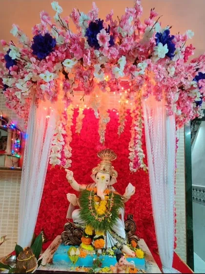 This cherry blossom-themed decor combines pink and white artificial flowers with a red backdrop and fairy lights. It's a vibrant and modern way to welcome Bappa into your home.