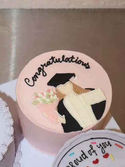 This lunchbox cake features a hand-piped illustration of a graduate holding a bouquet, a personal and thoughtful way to say congratulations.