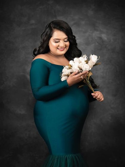 A soft and gentle portrait of a client in a teal gown, looking down at her bouquet of white roses. The dark, textured background makes the colors of her dress and flowers stand out.