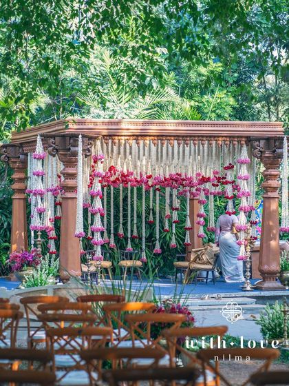 A view of the summer wedding mandap through the guest seating, showing the beautiful layers of flowers and foliage.
