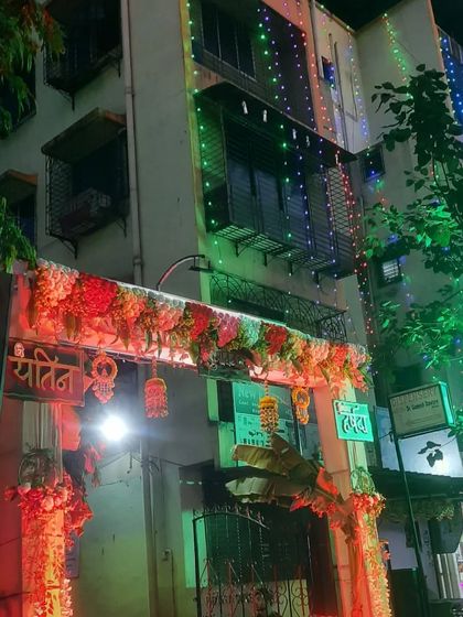 The exterior of a building decorated for a Haldi event, with a floral gate and colorful string lights illuminating the facade.