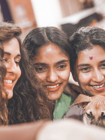 Three friends smile together with a puppy, capturing the community and connection forged at our events.