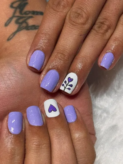 A cute and simple design on natural nails. This look features a soft lavender polish with a white accent nail adorned with a hand-painted heart and floral stem.