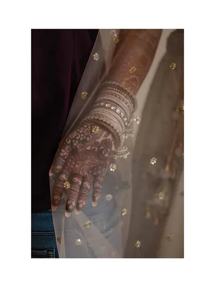 A beautiful detail shot of the bride's mehendi-adorned hand, seen through the sheer fabric of her dupatta.