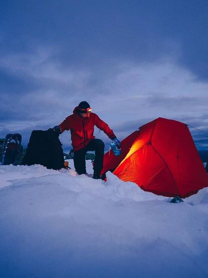 Setting up camp as the last light of day fades over a snow-covered landscape. This is a moment of preparation and anticipation for a quiet, cold night in the mountains.