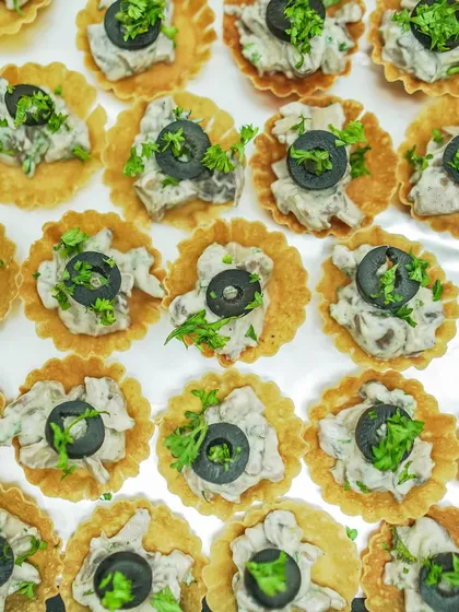 A top-down view of my creamy mushroom tarts, garnished with fresh parsley and black olives. I prepare these in large batches for events of any size.
