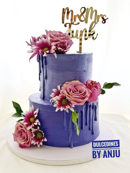 A bold and beautiful two-tier wedding cake in a striking purple hue. The dripping ganache and arrangement of fresh flowers add a touch of modern drama.