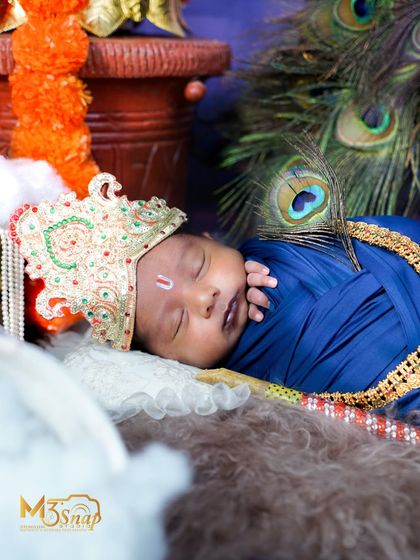 A close-up of a newborn dressed as baby Krishna, sleeping peacefully. The details of the crown and the peacock feather are exquisite.