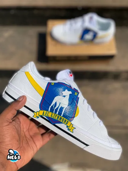 A hand-held shot of the AFC Richmond sneaker, displaying the detailed, hand-painted team crest over the swoosh.