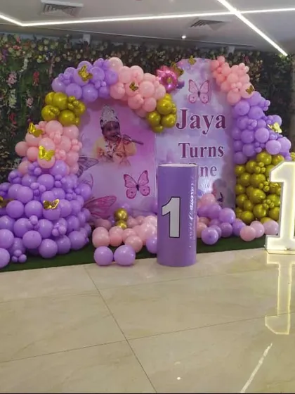 A beautiful butterfly-themed first birthday for Jaya. This setup, perfect for a hotel lobby or banquet hall, features a large balloon arch in purple, pink, and gold against a backdrop of green foliage.