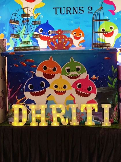 A close-up of a Baby Shark-themed setup, showing the character-printed plinths and 'DHRITI' marquee letters.