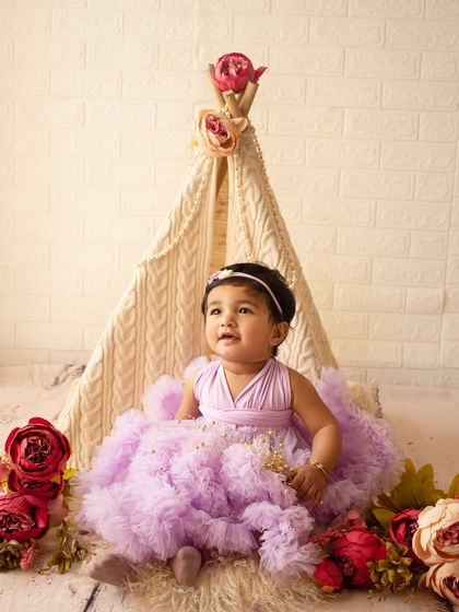 Miss "Onederful" in a dreamy lavender dress, sitting in front of a floral teepee for her first birthday photos.