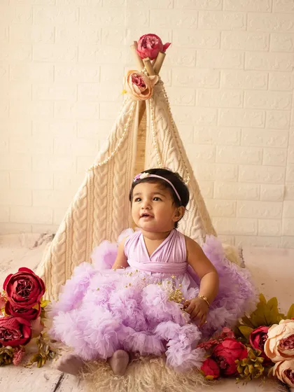 A dreamy first birthday setup with a lace teepee and floral decorations for a beautiful baby girl in a lavender dress.