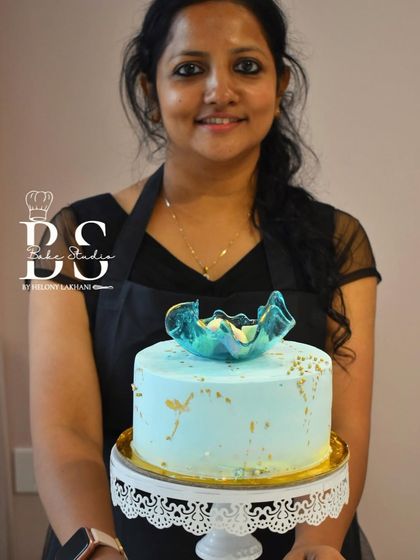 A student holding her elegant light blue whipped cream cake, topped with a delicate, hand-pulled isomalt sculpture.