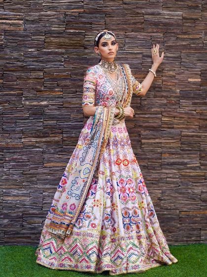 A full-length view of a stunningly vibrant, multi-coloured lehenga. The makeup is kept fresh and glowing to balance the intricate outfit, with a focus on clean skin and beautifully defined eyes.