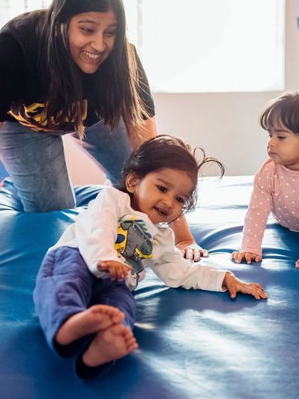 An instructor smiles as she guides two toddlers in a gentle crawling exercise on a soft mat. This foundational movement helps build core strength and coordination, preparing them for more complex skills later on.