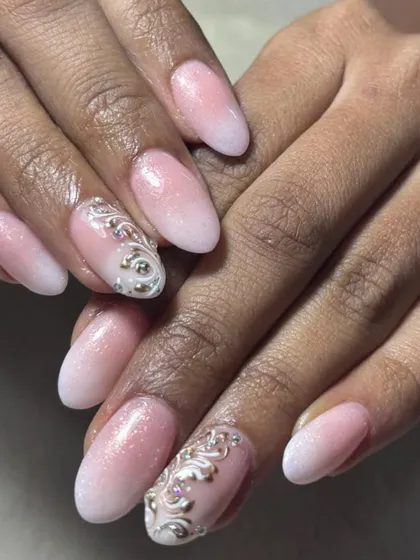 A beautiful example of ombre bridal nails. The soft fade from pink to white is accented with delicate, shimmering silver scrollwork and crystals, creating a sophisticated and timeless look for any bride.