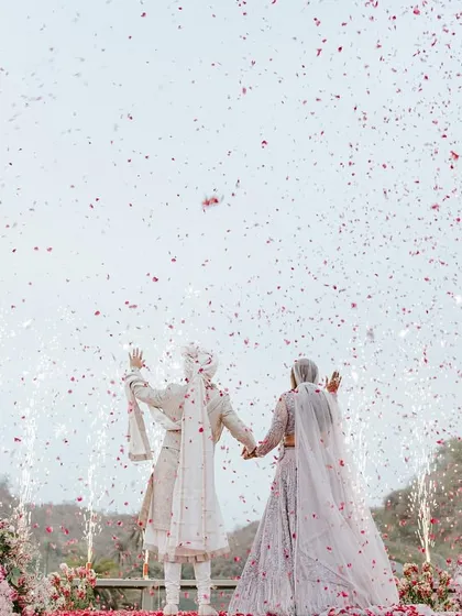 Two hearts, one promise, and a backdrop that felt just as timeless. The couple exchanges garlands on a bridge, surrounded by floral towers, as confetti rains down.
