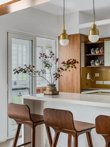 This kitchen from our 'Pepper and Coffee' project features a breakfast bar with warm wood tones, brass pendant lights, and mustard yellow tiles, creating an inviting and stylish space.