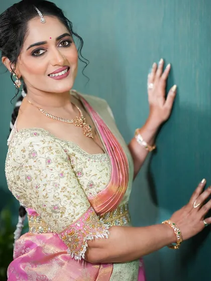 A close-up of a client wearing a custom hand-embroidered blouse. The pale green fabric is adorned with delicate floral threadwork in shades of pink and gold, perfectly matching her saree.
