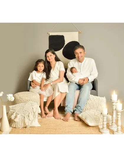This full family portrait showcases a modern, boho-chic studio setup with neutral tones and soft lighting. It captures a serene and stylish moment with the parents, older sister, and newborn together.