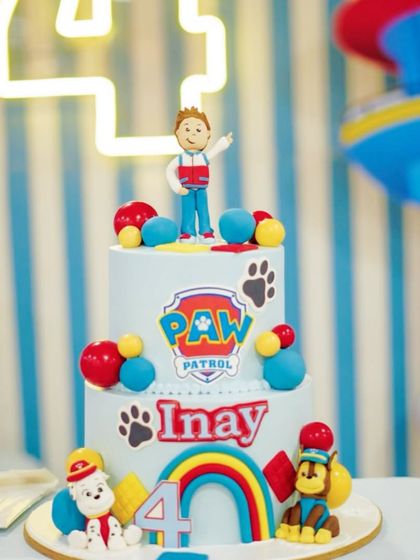 A fantastic Paw Patrol themed birthday cake for Inay. The cake is adorned with edible figures of Ryder, Marshall, and Chase, set against a backdrop of a neon '4' and a balloon arch.
