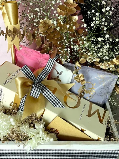 A detailed shot of the birthday essentials hamper. You can see the box of Moët & Chandon champagne and other gourmet snacks nestled among the golden-hued floral arrangement.
