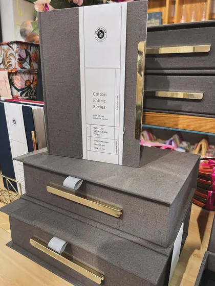 A stack of our Colton Fabric series keepsake boxes and a matching notebook. The design is minimal, allowing the quality of the materials to shine through.