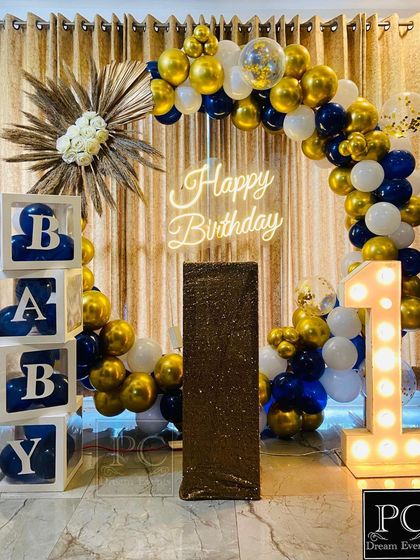 A clear, well-lit view of the sophisticated blue and gold first birthday setup. The dried palm leaf accent adds a modern, bohemian touch to the classic balloon and neon sign combination.