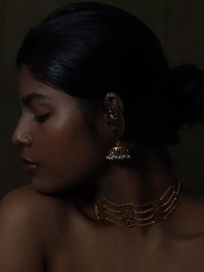 Focusing on a single piece, this shot highlights the intricate design of the jhumka earring. The dark background makes the gold stand out.