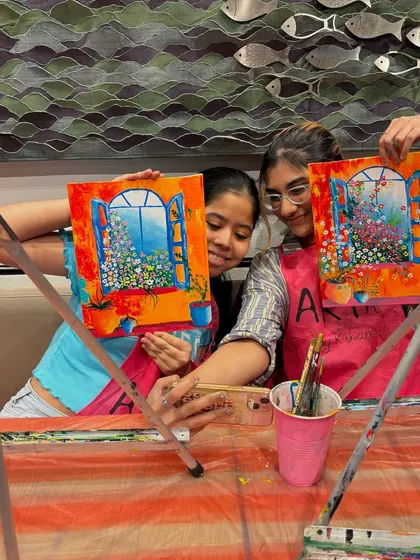 Two young participants taking a selfie with their vibrant window paintings. My workshops are a great place for friends to hang out and do something creative.