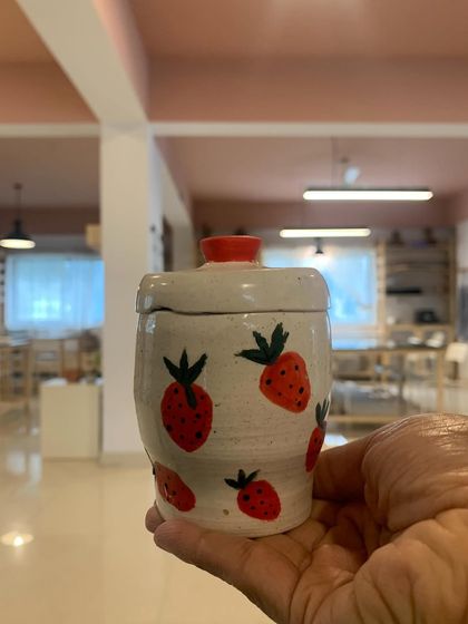This sweet, hand-painted strawberry jar is another wonderful creation from one of our students. It’s a cheerful and charming piece that brightens up any space.
