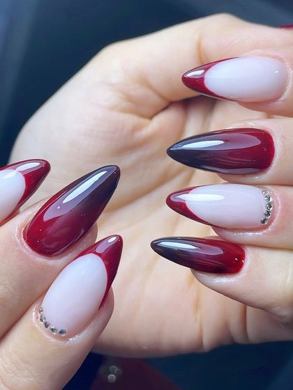 Glossy maroon tips with a side of sparkle. This stiletto set features a deep, vampy red V-French, with a delicate line of crystals at the base of the accent nail.