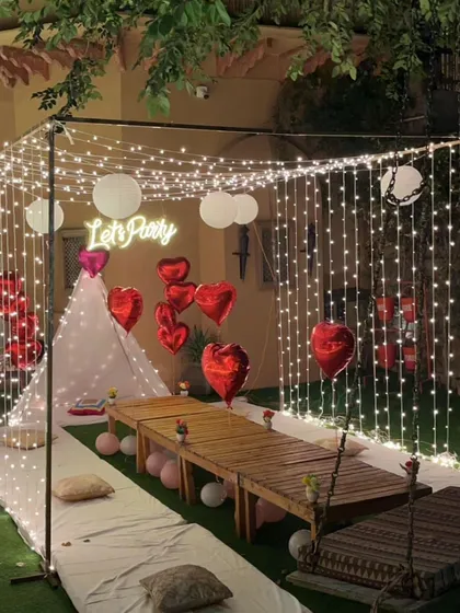 A full view of the cabana party setup, framed by a curtain of fairy lights. This perspective shows the complete arrangement, including the tent, low table, and surrounding decor.