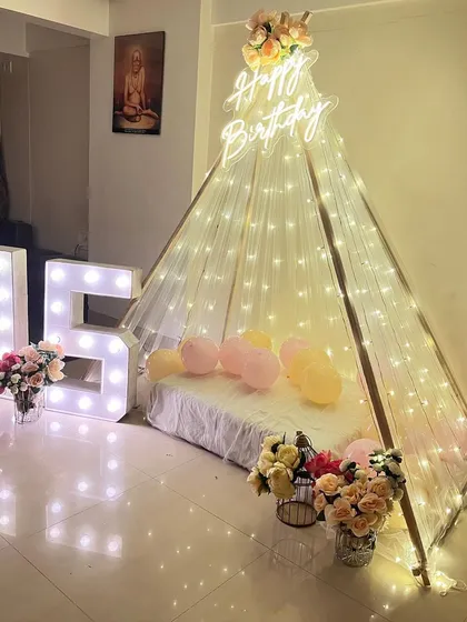 A cozy and dreamy 'Sweet 16' celebration. We set up an elegant teepee canopy draped with fairy lights, paired with light-up marquee numbers and beautiful flower arrangements for an intimate and memorable birthday surprise at home.