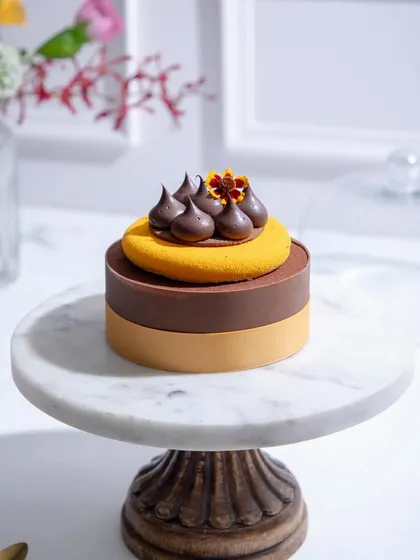 A sophisticated two-toned entremet in shades of brown and yellow, topped with chocolate quenelles and a marigold flower.
