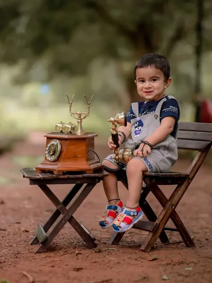 A proud, happy smile from baby Ishan during his vintage-themed photoshoot. The soft, blurred background keeps the focus entirely on his charming expression and the classic telephone prop.