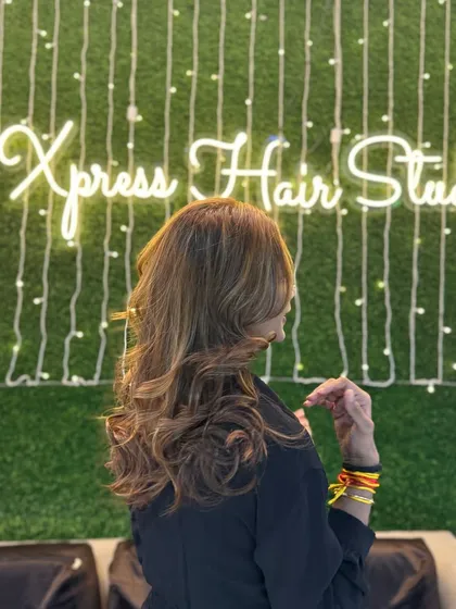 This is a great example of how lighting can showcase a hair color. The soft highlights and waves look fantastic against the backdrop of the Xpress Hair Studio neon sign.