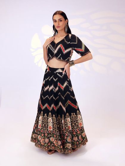 This full-length view showcases the entire black georgette lehenga, highlighting the contrast between the chevron print and the dense floral embroidery at the bottom.