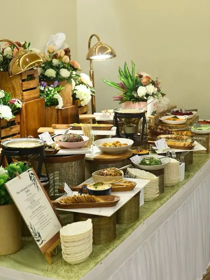 A comprehensive view of a diverse buffet spread, featuring both hot and cold dishes. The rustic wooden crates and floral arrangements add height and visual interest to the presentation.