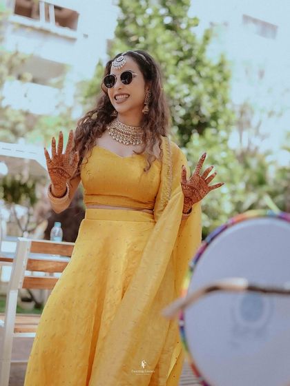 A fun, candid shot of the bride with her henna-adorned hands, dancing and enjoying the music at her Haldi or Mehendi party.